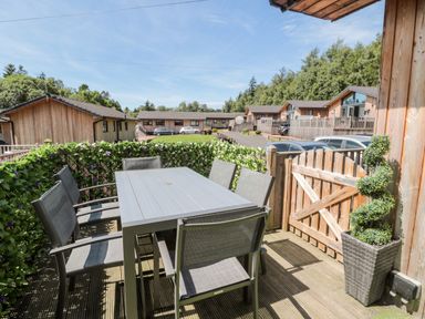 An outdoor patio area with a rectangular table and six chairs surrounded by wooden fencing and greenery at Lodge 32 Otterburn
