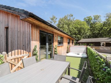 An outdoor patio area with a table and chairs and a hot tub beside a wooden building at Lodge 32 in Otterburn