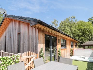 An outdoor wooden patio with a table and chairs a hot tub and a wooden building at Lodge 32 in Otterburn