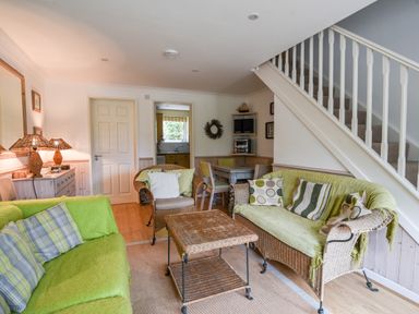 A living room with wicker sofas and chairs a coffee table a dining table and staircase at 52 Fernhill Heights in Charmouth