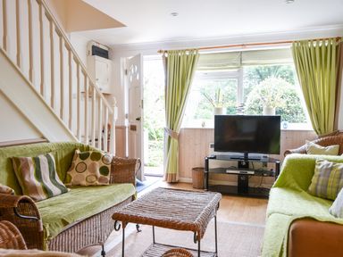 A living room with wicker sofas and a small table a television on a stand and an open door at 52 Fernhill Heights in Charmouth