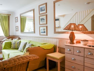 A living room with green curtains sofas wicker chair and a wooden dresser with a lamp at 52 Fernhill Heights in Charmouth