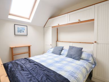 A bedroom with a bed under a skylight and white built-in cupboards at 52 Fernhill Heights in Charmouth