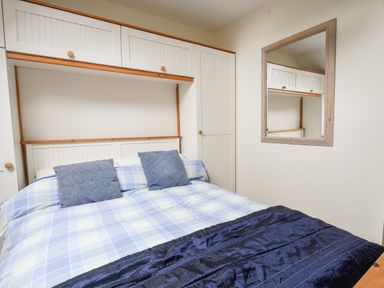 A bedroom with a bed with blue and white checked bedding and two blue pillows with built-in white cupboards and a mirror on the wall at 52 Fernhill Heights in Charmouth