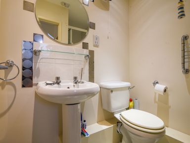 A bathroom with a pedestal sink and round mirror above it a toilet with cleaning supplies and toilet paper at 52 Fernhill Heights Charmouth