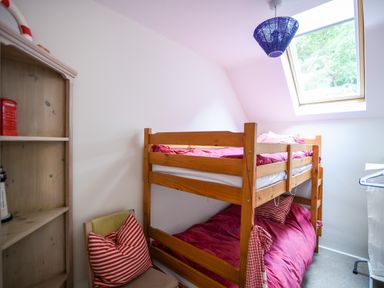 A small bedroom with a wooden bunk bed red bedding a chair with striped pillows a wooden shelf and a skylight window at 52 Fernhill Heights in Charmouth