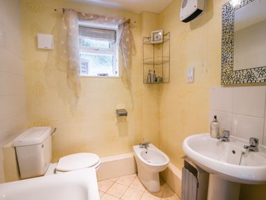 A bathroom with a toilet bidet sink mirror and window at 52 Fernhill Heights Charmouth