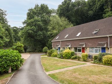 A row of houses with sloped roofs next to a paved path and green trees at 52 Fernhill Heights in Charmouth