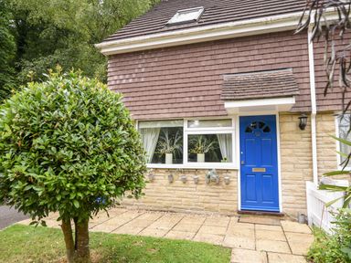 Front view of a house with a blue door and a small garden with a tree at 52 Fernhill Heights Charmouth