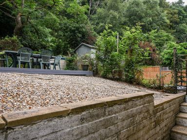 A garden area with a gravel surface chairs and a table near a shed and trees at 52 Fernhill Heights in Charmouth