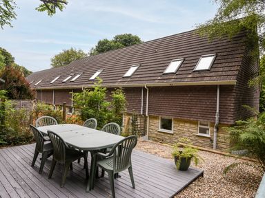 A patio with a table and six chairs next to a building with multiple skylights at 52 Fernhill Heights in Charmouth