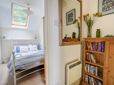 A bedroom with a bed under a skylight and a hallway with a wooden bookshelf mirror and a heater at 52 Fernhill Heights in Charmouth