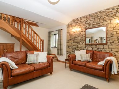 A living room with two brown leather sofas, a stone wall with a mirror, and wooden stairs at Bullfinch Cottage in Kingsland