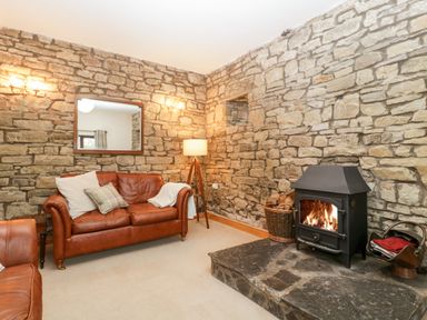 A living room with stone walls a brown leather sofa a fireplace and a floor lamp at Bullfinch Cottage in Kingsland