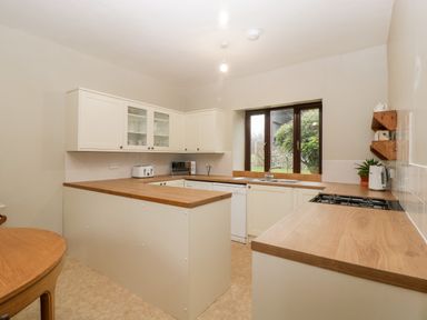 A kitchen with cream cabinets wooden countertops a window sink dishwasher microwave toaster and kettle at Bullfinch Cottage in Kingsland