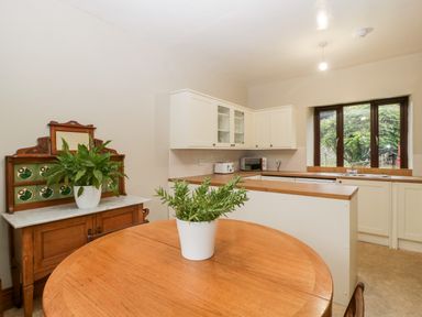 A kitchen with white cabinets a wooden dining table with a plant and a wooden sideboard with a plant at Bullfinch Cottage in Kingsland