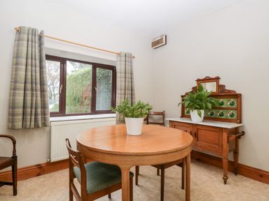 A dining room with a round wooden table and chairs a sideboard with a plant and a window with plaid curtains at Bullfinch Cottage in Kingsland