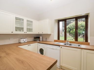 A kitchen with white cabinets wooden countertops a stainless steel sink a toaster microwave washing machine and dishwasher at Bullfinch Cottage in Kingsland