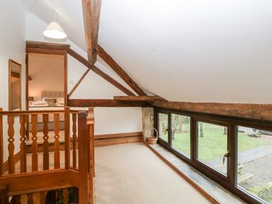 An upstairs landing area with wooden beams and large windows overlooking a garden at Bullfinch Cottage in Kingsland