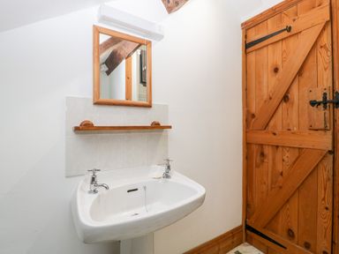 A bathroom sink with two taps below a wooden framed mirror and shelf next to a wooden door at Bullfinch Cottage in Kingsland