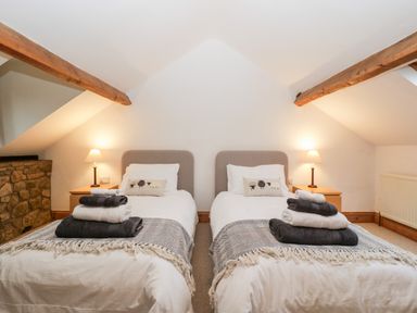 A bedroom with two single beds with folded towels on each bed and two bedside tables with lamps at Bullfinch Cottage in Kingsland