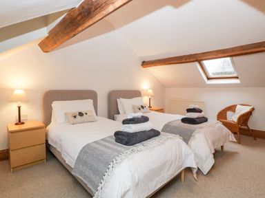 A bedroom with two single beds wooden nightstands lamps a wicker chair and skylight windows at Bullfinch Cottage in Kingsland