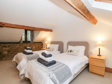 A bedroom with two single beds nightstands lamps and wooden beams at Bullfinch Cottage in Kingsland