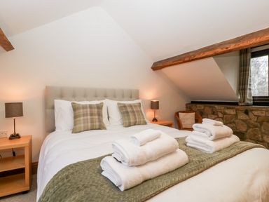 A bedroom with a bed with folded towels on it two bedside tables with lamps and a window with plaid curtains at Bullfinch Cottage in Kingsland