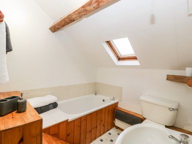 A bathroom with a wooden paneled bathtub a toilet a sink and a skylight window at Bullfinch Cottage in Kingsland