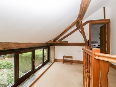 An upstairs landing area with wooden beams a small stool and windows showing garden view at Bullfinch Cottage in Kingsland