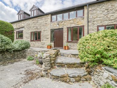 Stone cottage exterior with wooden door stone steps and shrubs at Bullfinch Cottage in Kingsland