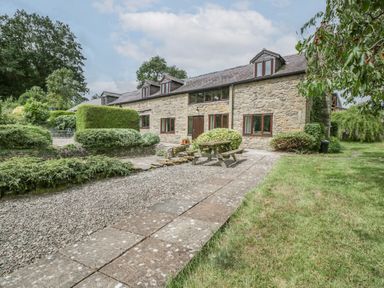 A stone house with wooden windows and a picnic table outside surrounded by bushes and trees at Bullfinch Cottage in Kingsland