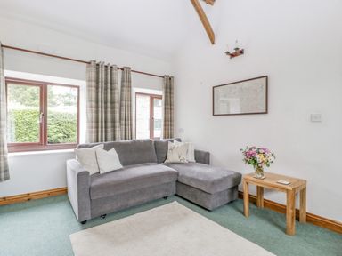 A living room with a grey sofa cushions wooden side table and flowers at Fieldfare in Kingsland