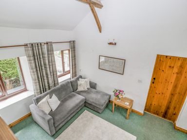 A sitting area with a gray sofa pillows side table with flowers wood door and windows with checked curtains at Fieldfare in Kingsland
