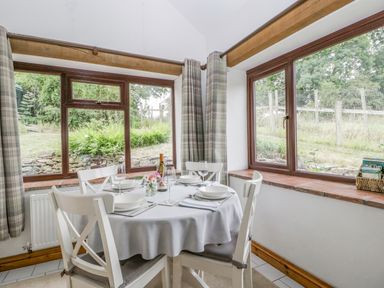 A dining area with a round table set for four by corner windows with plaid curtains at Fieldfare in Kingsland