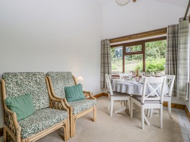A dining area with a round table set for four and two patterned armchairs with green cushions at Fieldfare in Kingsland