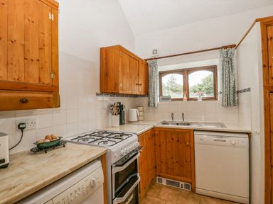 A kitchen with wooden cabinets a gas stove a dishwasher a sink under a window and kitchen utensils at Fieldfare Kingsland