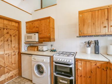 A kitchen with wooden cabinets a washing machine a microwave an oven and cooking utensils at Fieldfare Kingsland