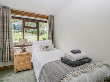 A bedroom with a single bed, bedside table with lamp, and window with curtains at Fieldfare in Kingsland