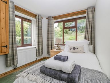 A bedroom with a single bed towels on the bed and two windows with curtains at Fieldfare in Kingsland