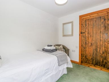 A bedroom with a single bed white bedding folded towels a chair with a cushion a mirror and a wooden door at Fieldfare in Kingsland