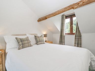 A bedroom with a bed with white linens and plaid pillows under a wooden beam next to a window with plaid curtains at Fieldfare in Kingsland