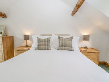 A bedroom with a double bed two plaid pillows two bedside tables with lamps and a wooden dresser at Fieldfare in Kingsland