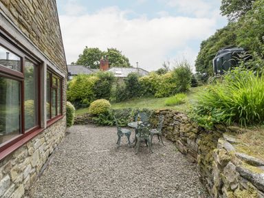 An outdoor gravel patio area with a metal table and four chairs next to a stone building at Fieldfare in Kingsland