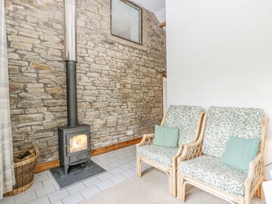 A seating area with two patterned armchairs and a wood-burning stove against a stone wall at Fieldfare in Kingsland