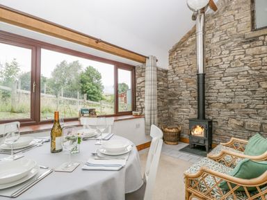 A dining area with a set table next to large windows and a stone wall with a wood burning stove at Fieldfare in Kingsland