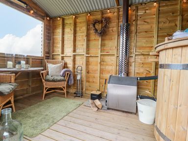 A wooden room with wicker chairs a table a small stove logs and a hot tub at Heather Hut at Copy House Hideaway in Earby