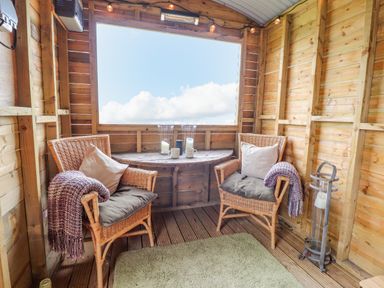 A wooden cabin room with two wicker chairs a round table and a large window at Heather Hut at Copy House Hideaway in Earby