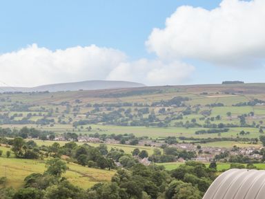 A rural landscape with fields trees and a village under a partly cloudy sky at Heather Hut at Copy House Hideaway in Earby