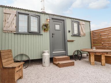 A small green cabin with grey trim and wood shutters with wooden steps and outdoor wooden furniture at Heather Hut at Copy House Hideaway in Earby